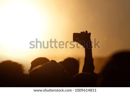 Silhouette of smartphone in a hand over crowd