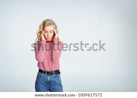 Portrait of attractive blond woman in a striped sweater and jeans. Girl posing on white background. Freelancer's concept. Close up. The girl holds hands the head. Headache.