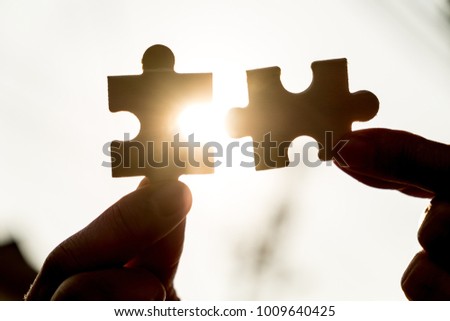 Two hands connect couple puzzle piece with sunset background.