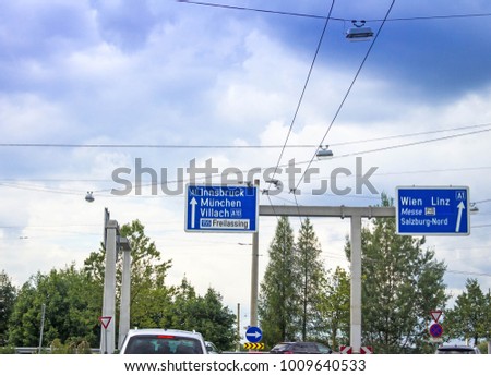 Busy traffic and an exit sign for 1 and 10 highways in the direction to Innsbruck, Munich,Munchen, Villach, Freilassing, Wien, Linz,Messe, Vienna on cloudy summer sky background. Salzburg. Austria