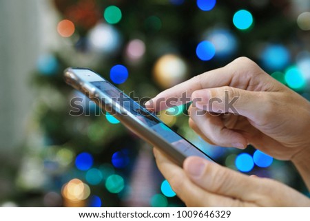 People hand using smartphone for shopping on winter holidays blur Christmas tree background