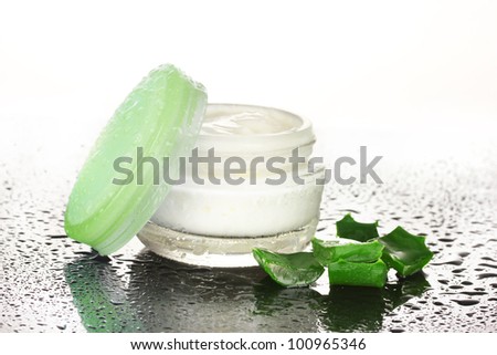 Opened glass jar of cream and aloe on black and white background with water droplets
