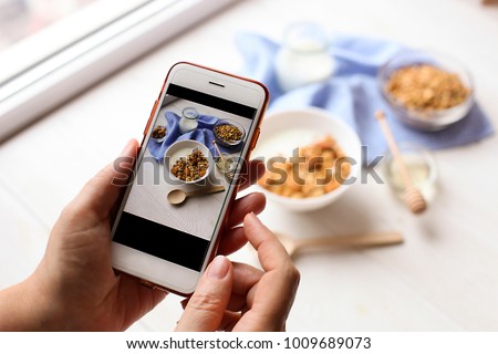 Young woman food blogger takes photo for blog, pic of bowl with Greek yogurt homemade granola, mixed nuts, almond, cashew, hazelnut. Healthy vegetarian protein diet breakfast. Selective focus, closeup