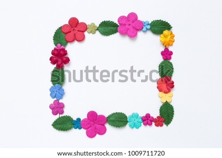 Colorful paper flower and green leaf arrange in frame shape on white paper texture background, flower card concept