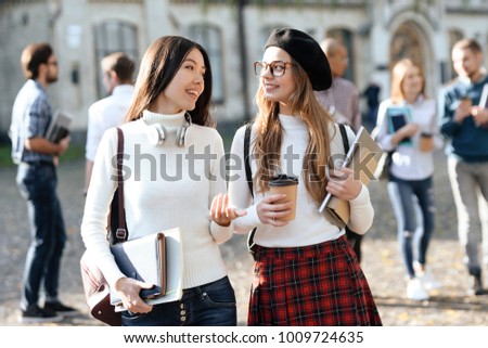 Two girls together communicate in the courtyard of the university. It's sunny outside. The students have a good mood.