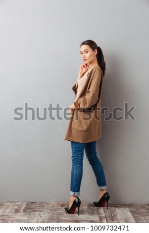 Side view full length of a pretty young asian woman posing while standing over gray background