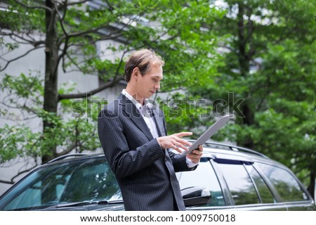 Young male caucasian using tablet PC in front of a car.