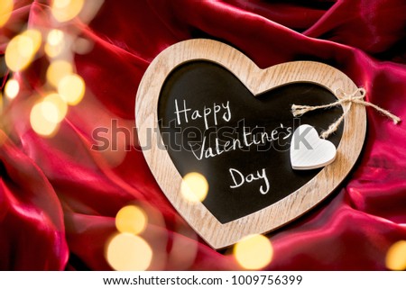 Happy Valentine's Day on heart-shaped blackboard, red background and fairy lights