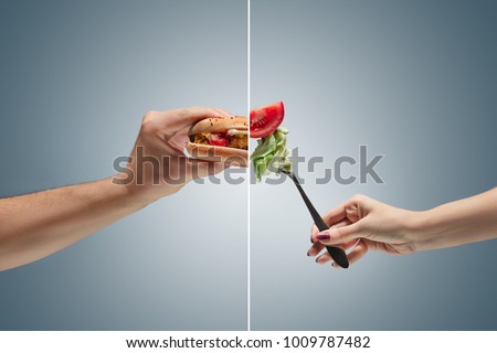 Male and female hands holding tasty hamburger and fresh vegetables on a blue background. concept of confrontation, differences in taste and preference. concept of healthy and unhealthy food
