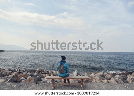 A woman is sitting on the bench and looking at the sea.