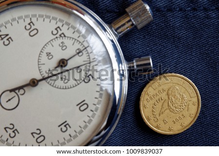 Euro coin with a denomination of 10 euro cents (back side) and stopwatch on old blue denim backdrop - business background