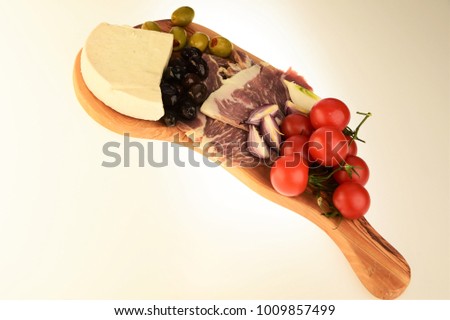 A wooden plateau with cheese, tomatoes, green olives, black olives and meat appetizers