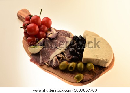 A wooden plateau with cheese, tomatoes, green olives, black olives and meat appetizers