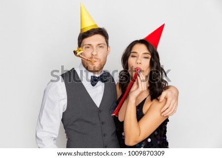birthday, celebration and holidays concept - happy couple with party blowers and caps having fun