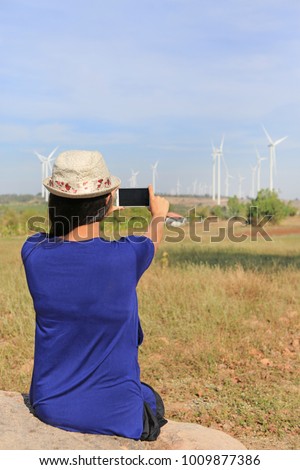 Young woman taking photos of wind turbine field.