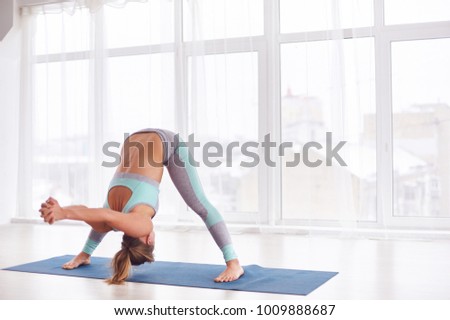 Beautiful young woman practices yoga asana Prasarita Padottanasana at the yoga class