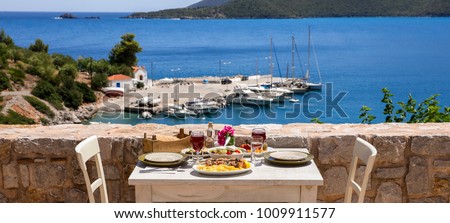 A table served for two with chicken souvlaki and french fries, greek salad, snacks and drinks on the summer terrace of the hotel room by the seascape, beautiful summer greek holidays concept.