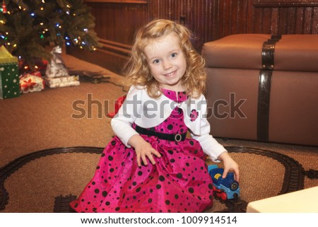 Cute Caucasian blond curly hair girl is playing with a train toy indoor