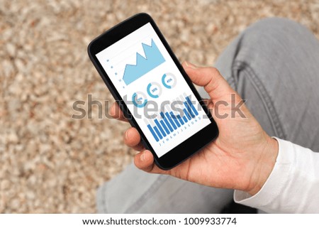 Hand holding smart phone with graphs and charts elements on screen. All screen content is designed by me