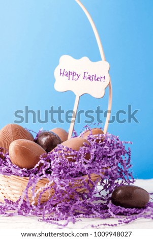 Image of chicken, chocolate eggs, purple decorative paper in basket ,wish for happy Easter