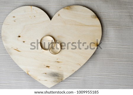 Gold wedding rings on a wooden heart. Bright, glittering, glamorous, fashionable, expensive hearts made of wood with adornments for Valentine's Day against a background of beige fabric.