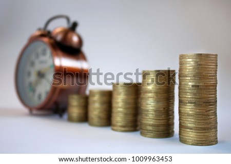 Rows coin in fount of alarm clock on the white background for business concept,finance,tax time  for currency and financial business investment, loans to planned investment. Time is money. 