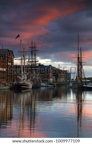 Tall shops moored at Gloucester docks under a red sunset sky