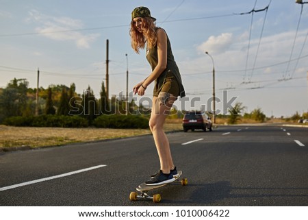Cheerful young girl with tattoos riding on longboard on the road in the city in sunny weather. Extreme sports. Lifestyle, hobby, freedom, self expression
