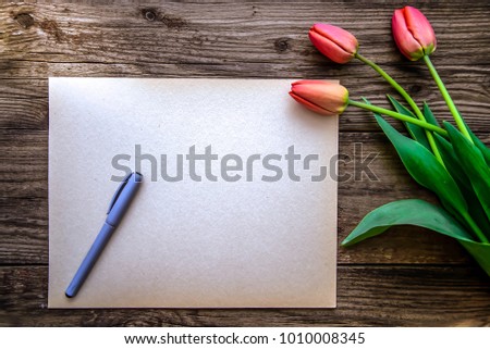 Romantic beautiful spring picture with three red tulips and blue ballpoint pen on a piece of paper on a wooden surface with copyspace