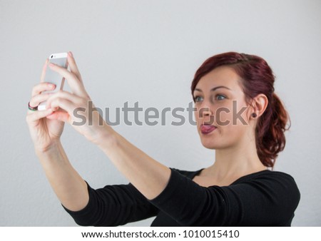 A young girl uses a cell phone to take a front camera, a white background, a studio, facial expressions