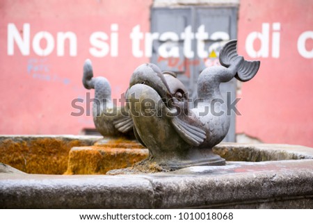 Beautiful fish shaped sculpture, part of an outdoor fountain in a public square in Salerno, Italy, one of the symbols of this nice city. On the wall in the background it's written: "It's not about..."