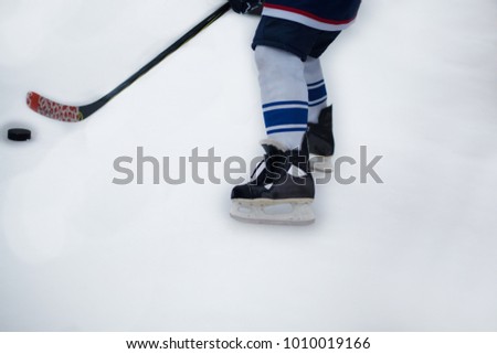 Kids hockey player legs on natural ice with hockey stick and puck