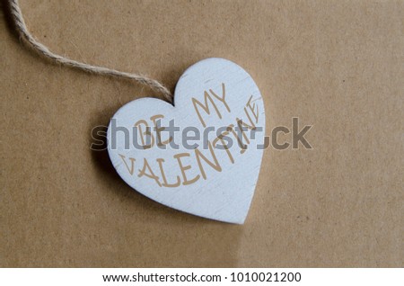 Wooden white heart shape with message text: BE MY VALENTINE. Top view on pendant romantic on cartoon.