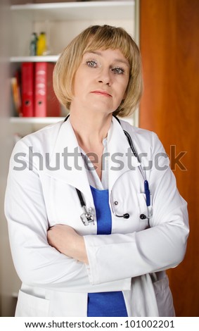 Mature woman doctor in white coat standind in front of shelf with medical files