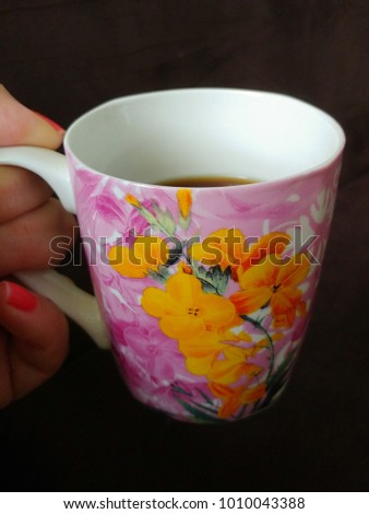 Female hand holding a flowery mug with coffee; dark background.