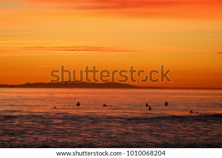 Sunset over the ocean with surfers in the water