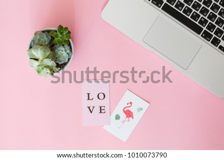 on a pink paper background lie a laptop, a flower succulent, cards with the inscription "Love" and flamingos