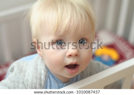 A small, blond boy 1.5 years old with blue eyes and a round face and a funny surprised emotions on the face.