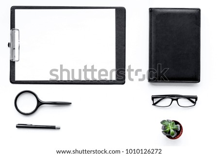 Strict work desk with pad, glasses, magnifiger, notebook, plant on white background top view copy space mock up