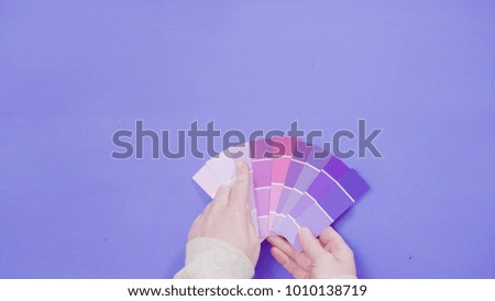 Hand holding paint swatches with shades of violet colors.