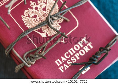 Russian passport wrapped in barbed wire on a blue textile background, close-up