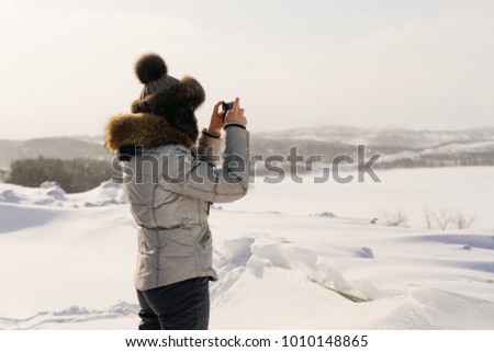 woman in winter suit photographing snow-covered field