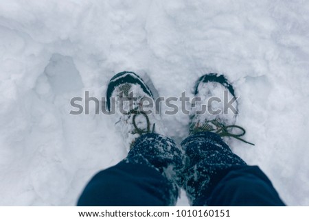 Photo of human feet in the snow in snow-covered boots with an empty white snowy background. View from above.