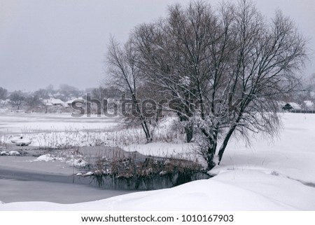 Photo of a winter landscape with a pond. A lot of snow, big snowdrifts, cloudy.