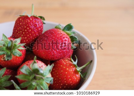 Fresh and juicy strawberries in a white ceramic bowl on a light wooden table