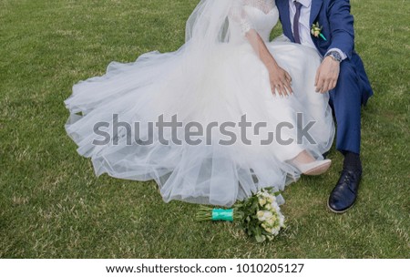 bride and groom are sitting on the grass