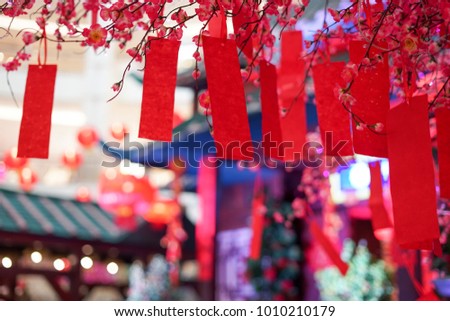 Close up shot of an artificial red and pick sakura flower with red paper note hanging on the sakura branch.Blur and bokeh background.Chinese New Year decoration.