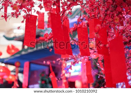 Close up shot of an artificial red and pick sakura flower with red paper note hanging on the sakura branch.Blur and bokeh background.Chinese New Year decoration.