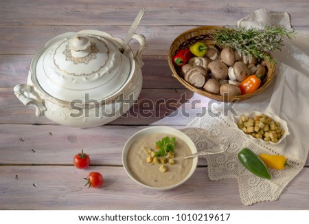 Fresh, mushroom soup-puree in a bowl, tureen, crouton and vegetables in a wicker basket on a wooden table close-up.   Royalty-Free Stock Photo #1010219617
