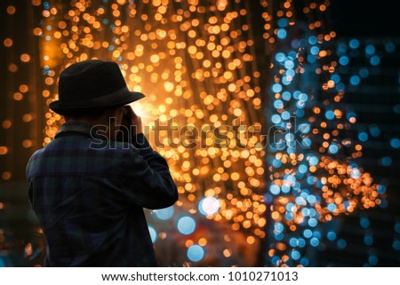 Young Asian tourist wearing black hat, silhouette, taking a photo, lighting bokeh background at night